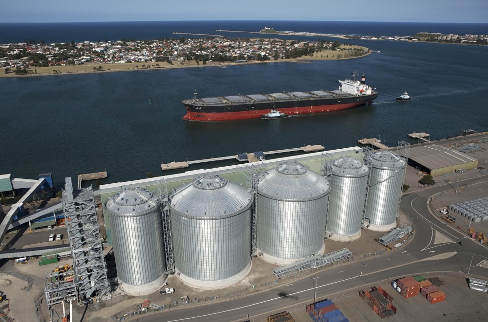 Aerial view of the Newcastle Agri Terminal silos with a bulk carrier arriving in the Newcastle shipping channel, Nobbys headland behind